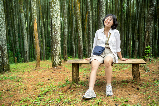 Asian woman sitting on the bench in the forest. Traveling activity