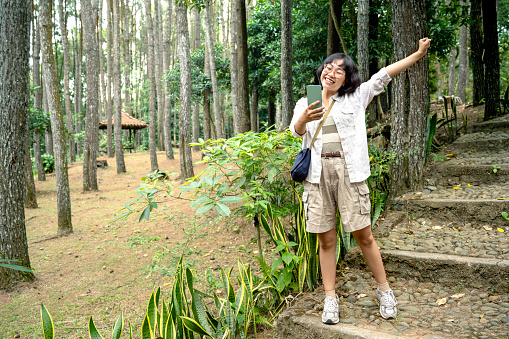 Asian woman using a mobile phone with a happy expression in the forest. Traveling activity