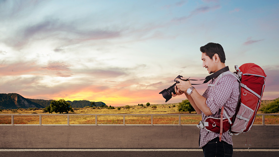 Asian man with a backpack holding the camera. World Photography Day
