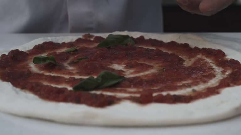 The entire making process of pizza; rolling out the dough, applying sauce and adding cheese and mint