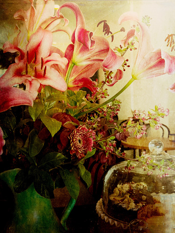 My original closeup photo of a bunch of bright flowers in a green vintage ceramic vase next to a freshly baked cake in a glass dome in a cafe, has been transformed using the Mextures app to bring a retro painterly still life effect to the image.
