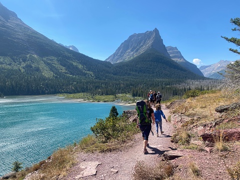 Glacier National Park, Montana, United States - August 26th, 2023: A group of hikers walking on three falls trail with Saint Mary Lake below and the mountains in the background, in Montana, USA.