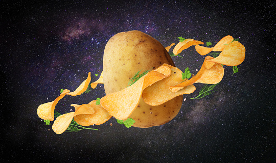 Potato surrounded by chips with greens in space