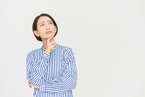 A gesture of a bob-haired Japanese woman wearing a blue striped shirt dress.She is thinking with her arms crossed.