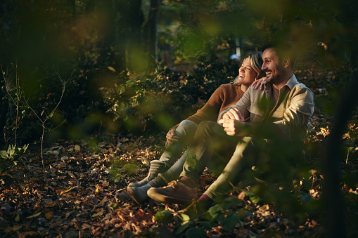 Happy couple enjoying while sitting in autumn leaves in the forest.