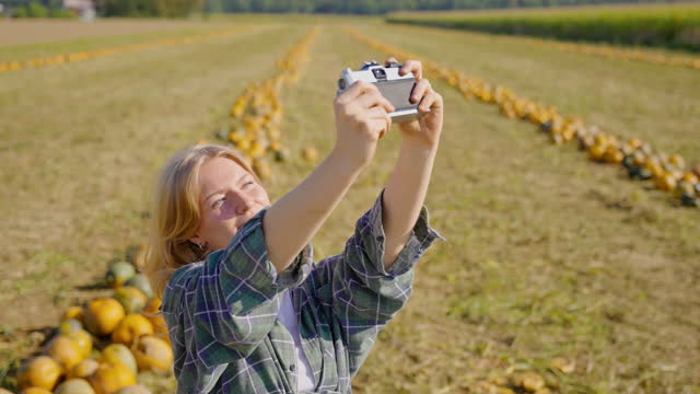 SLO MO Smiling Young Woman Taking Selfie With Harvested Pumpkins Using Retro Camera at Farm on Sunny Day