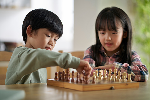 two asian children brother and sister sitting at table at home playing chess