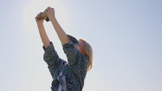 SLO MO Blond Young Woman Taking Selfie With Harvested Pumpkins Using Camera at Farm against Sunny Sky