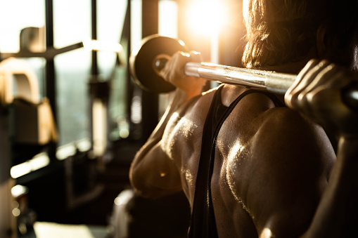 Close up of sweaty muscular build athlete doing back exercises with barbell in a gym.