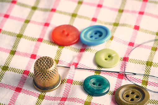 Sewing kit consisting needle, thimble and buttons fabric background