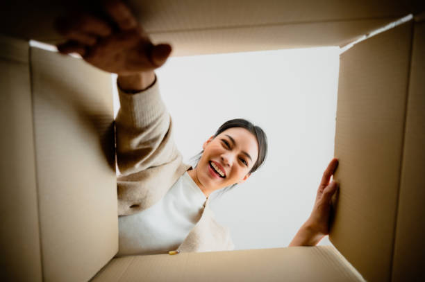 istock Surprised young asian woman unpacking. Opening carton box and looking inside. Packaging box, delivery service. Human emotions and facial expression 1675422676
