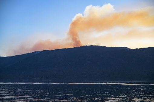 A scenic view of Okanagan Lake in British Columbia, Canada with a billowing smoke behind a mountain