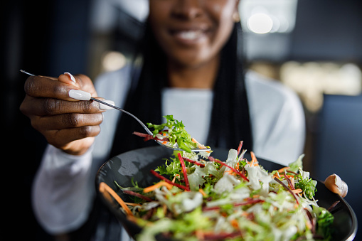 Close up of unrecognizable black woman holding a plate with multi-colored fresh salad.