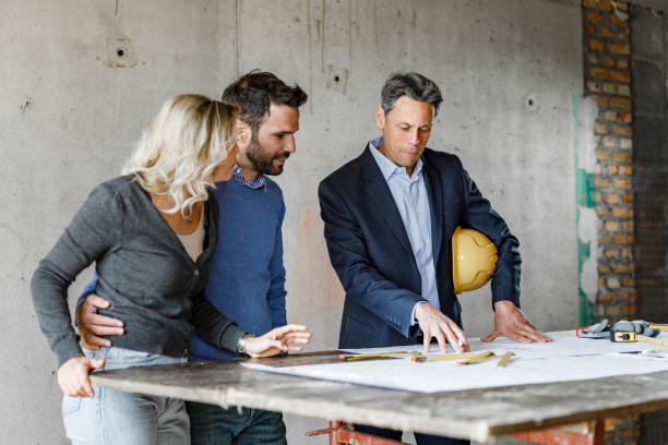 istock Young couple and their architect examining blueprints at construction site. 1675441393