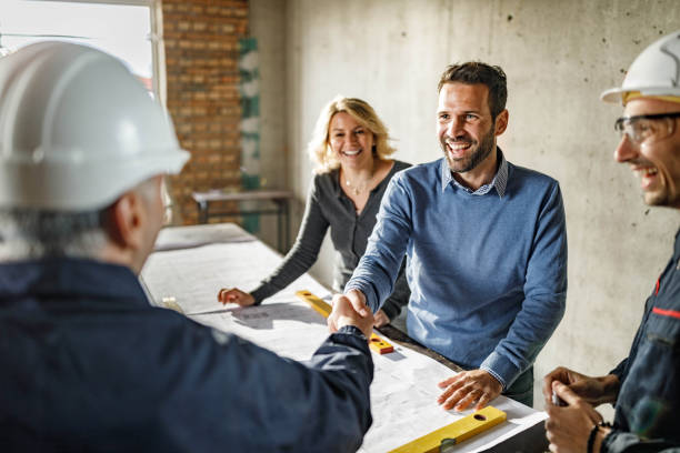 istock Happy couple closed a deal with manual workers at construction site. 1675442542