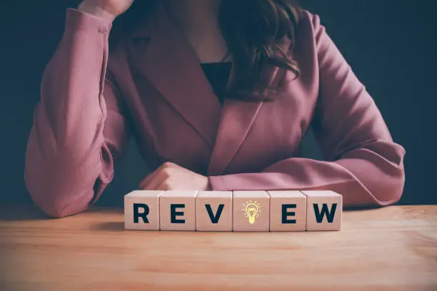 Photo of Businesswoman with Review text on wooden cube blocks. Concept of planning and development, improvement, business review for learning, review inspection assessment auditing, end of year business.