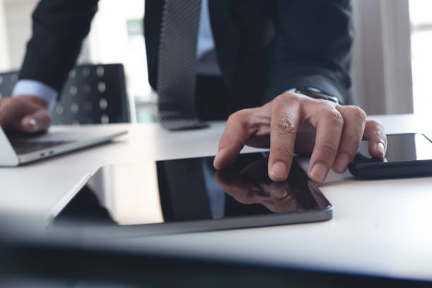 istock Businessman in black suit using digital tablet and  working on laptop computer on table at office. Business man finger touching on tablet screen at desk and suring the internet, close up 1675491002