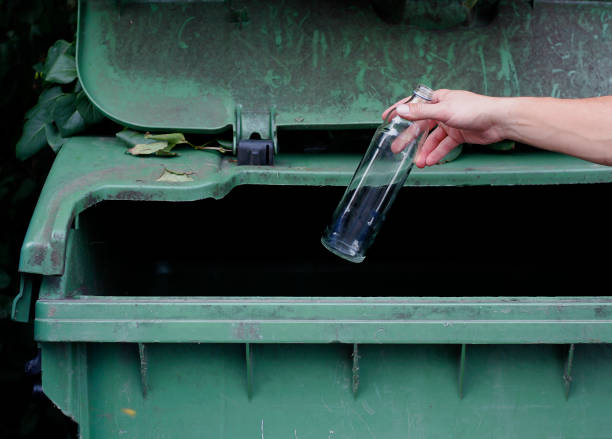 istock Caucasian man's hand throwing empty glass bottle into a green recycling container. Caring about environment, separating garbage into different containers. Recycling garbage concept. 1675514371