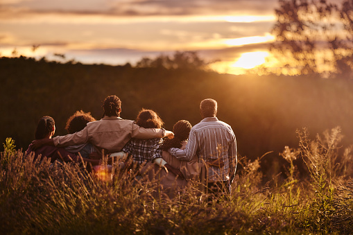 Rear view of African American multi-generation family standing embraced in nature and looking at sunset.