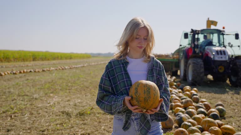 SLO MO Beautiful Young Female Farmer Holding Pumpkin while Walking In Front Of Combine Harvester at Farm