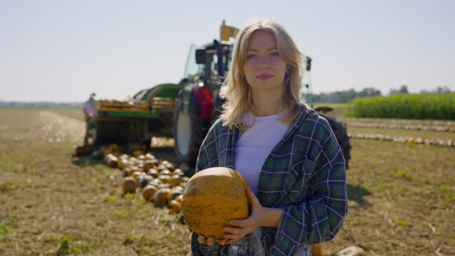 SLO MO Smiling Beautiful Female Farmer Holding Pumpkin while Standing In Front Of Combine Harvester At Farm