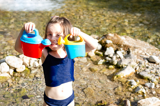 Happy girl holding toys cans in her hands and looking at camera at river