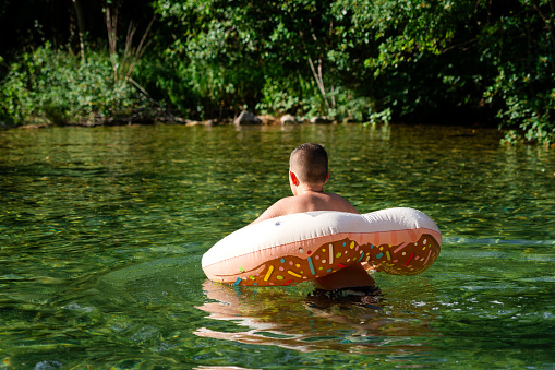 Rear view of boy in inflatable ring at river, full length