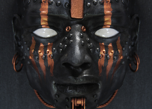 Black face sculpture. Close-up of portrait of a warrior with copper tribal makeup. Non-human creature with white eyes. Contemporary art.