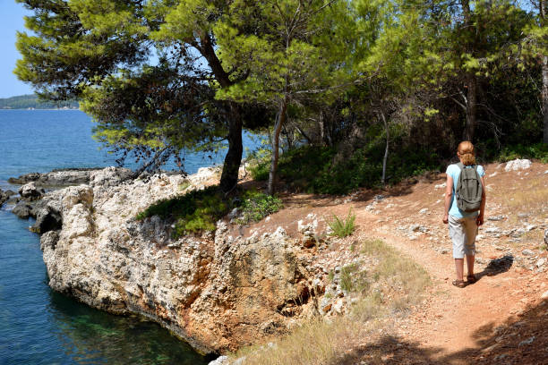 Woman with backpack walking on the coastal path near the sea and enjoying the nature. Back view. Travel and active lifestyle concept.