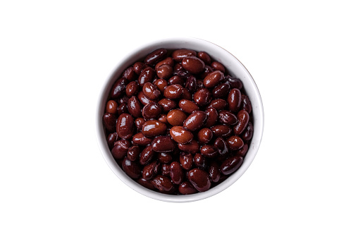 Black, canned beans in a white saucer against a dark concrete background. Ingrient for vegitarian cooking