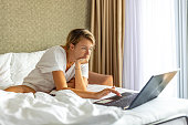 Woman using laptop computer sitting on bed at home