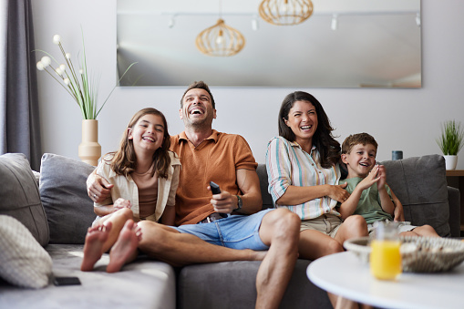 Cheerful parents and their kids having fun while watching a movie on sofa in the living room.