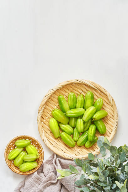 flat lay overhead top view green bilimbi kamias fruit in bamboo plate on white wood table background. green bilimbi kamias on white background. green bilimbi kamias on white food table light mood plano sobre la vista superior de la parte superior verde bilimbi kamias fruta en plato de bambú sobre fondo de mesa de madera blanca. bilimbi kamias verdes sobre fondo blanco. bilimbi verdes kamias en mesa de comida blanca estado de ánimo ligero