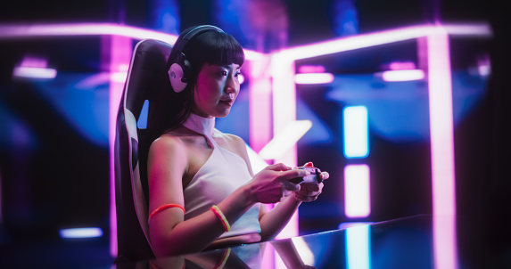 Japanese Female Playing Online Street Racing Simulator on a Computer. Footage of a Gamer Girl Sitting Behind a Table, Streaming Racing Gaming Content From a Futuristic Neon Room