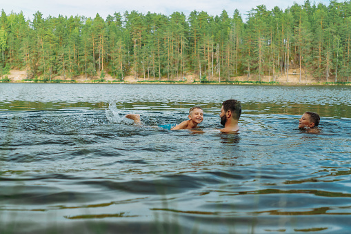 father and children swimming in forest lake. Man teaching son to swim. High quality photo