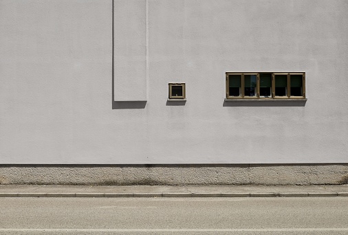 Small windows on gray plaster facade. Concrete sidewalk and urban street in front. Background for copy space.