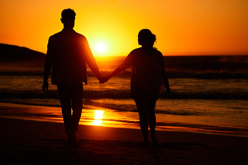 Ocean sunset, couple walking and beach water at night or woman and man love holding hands at sea summer vacation. Travel together, honeymoon silhouette and evening holiday sky sunlight in nature
