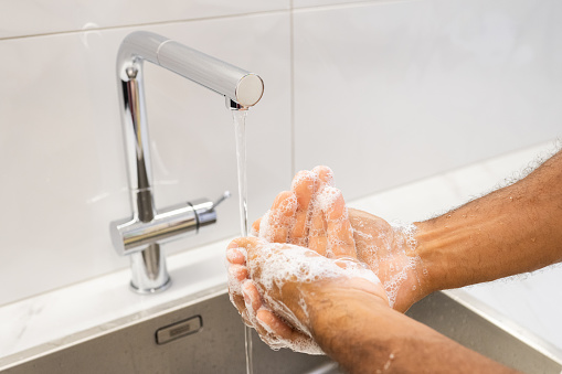 Close-up of man washing hands at kitchen sink.