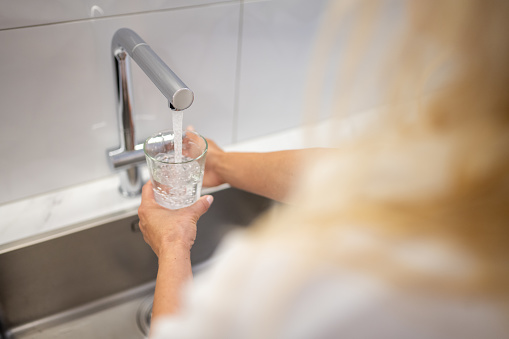 Woman filling glass of water at kitchen sink.