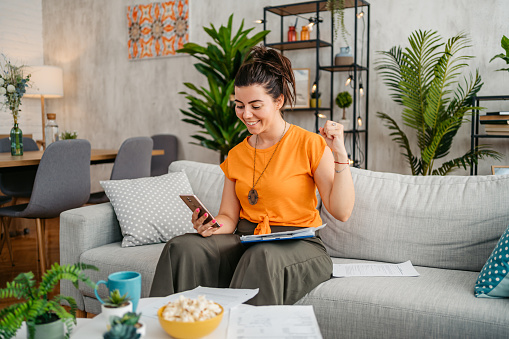 Happy young woman calculating her finances on a smart phone at home.