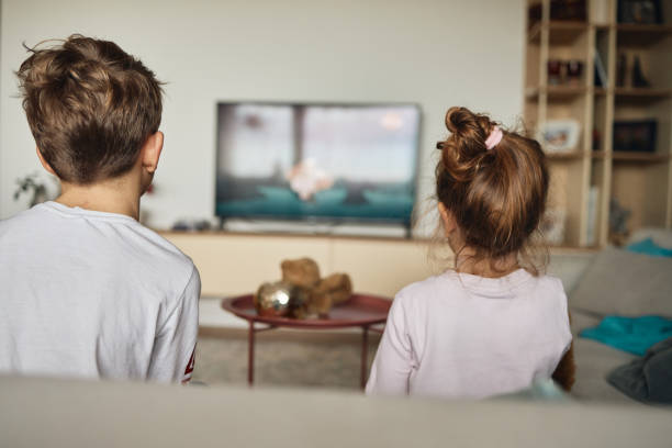 istock Boy and girl watching TV on sofa at home 1675722421