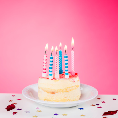 Birthday cake with candles standing on the table, isolated on pink background, square composition, copy space.