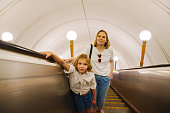 Mom and daughter ride up the escalator in the subway.