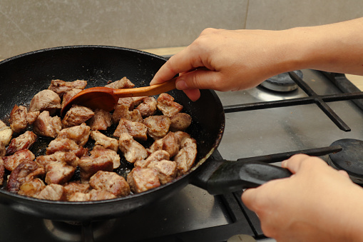 Woman mixing the meat in a frying pan shovel. Pan-fried meat, French fries. Close up of a pan with preparing of beef stroganoff