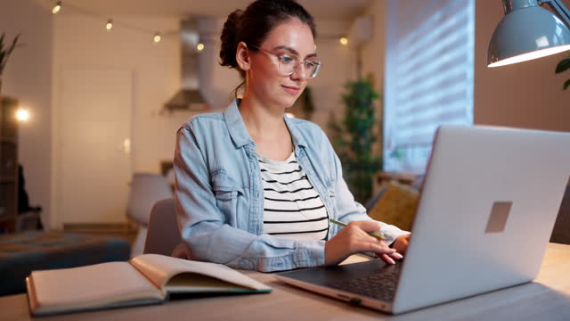 Modern young woman studying at home, while using laptop