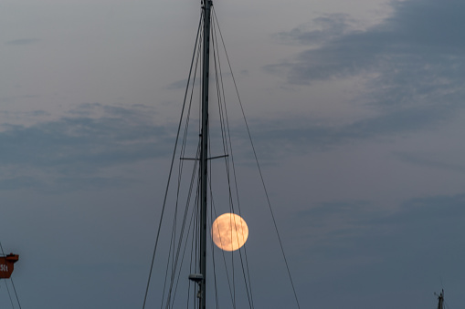 image of dusk sky of the orange full moon next to a ship mast