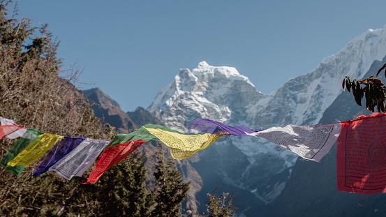A range of colorful flags blowing in the wind against a mountain backdrop.