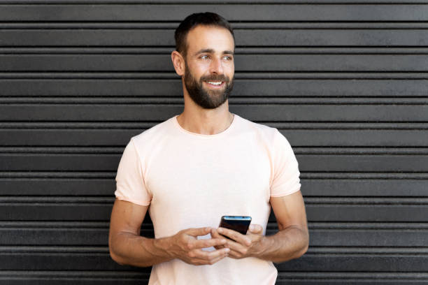 istock Smiling bearded man using mobile phone shopping online, text messaging standing on the street 1675780589