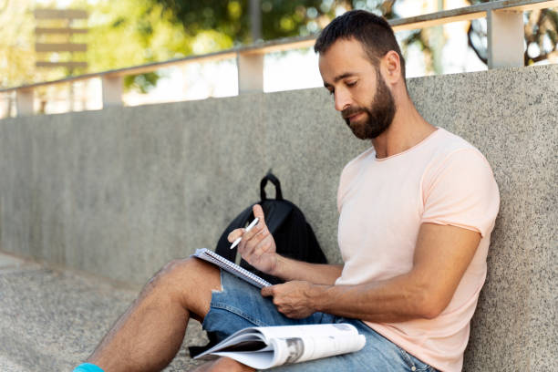 istock Pensive man holding paper notepad, taking notes, writing resume sitting on the street 1675780591