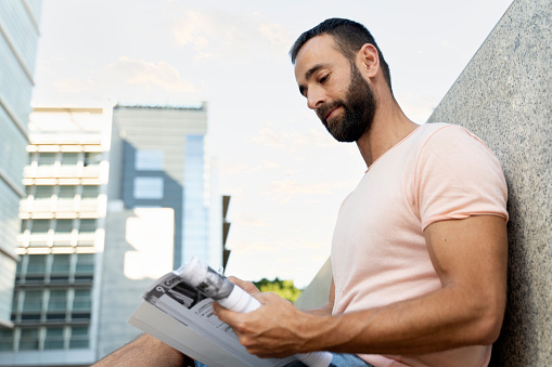 Pensive latin student studying, learning language, sitting in university campus, education concept. Handsome bearded man reading book outdoors